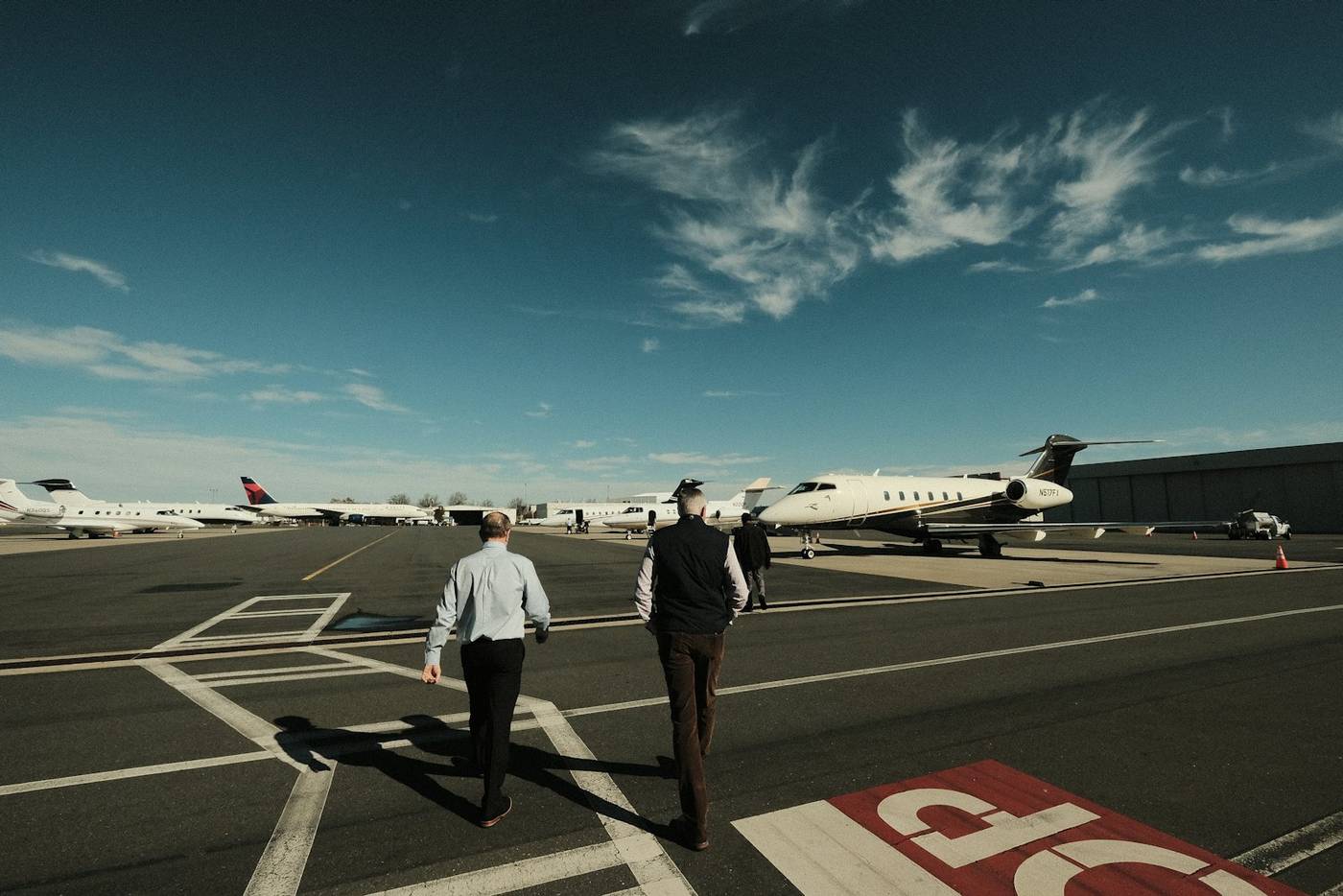 Two people walking across an airfield towards a private aircraft