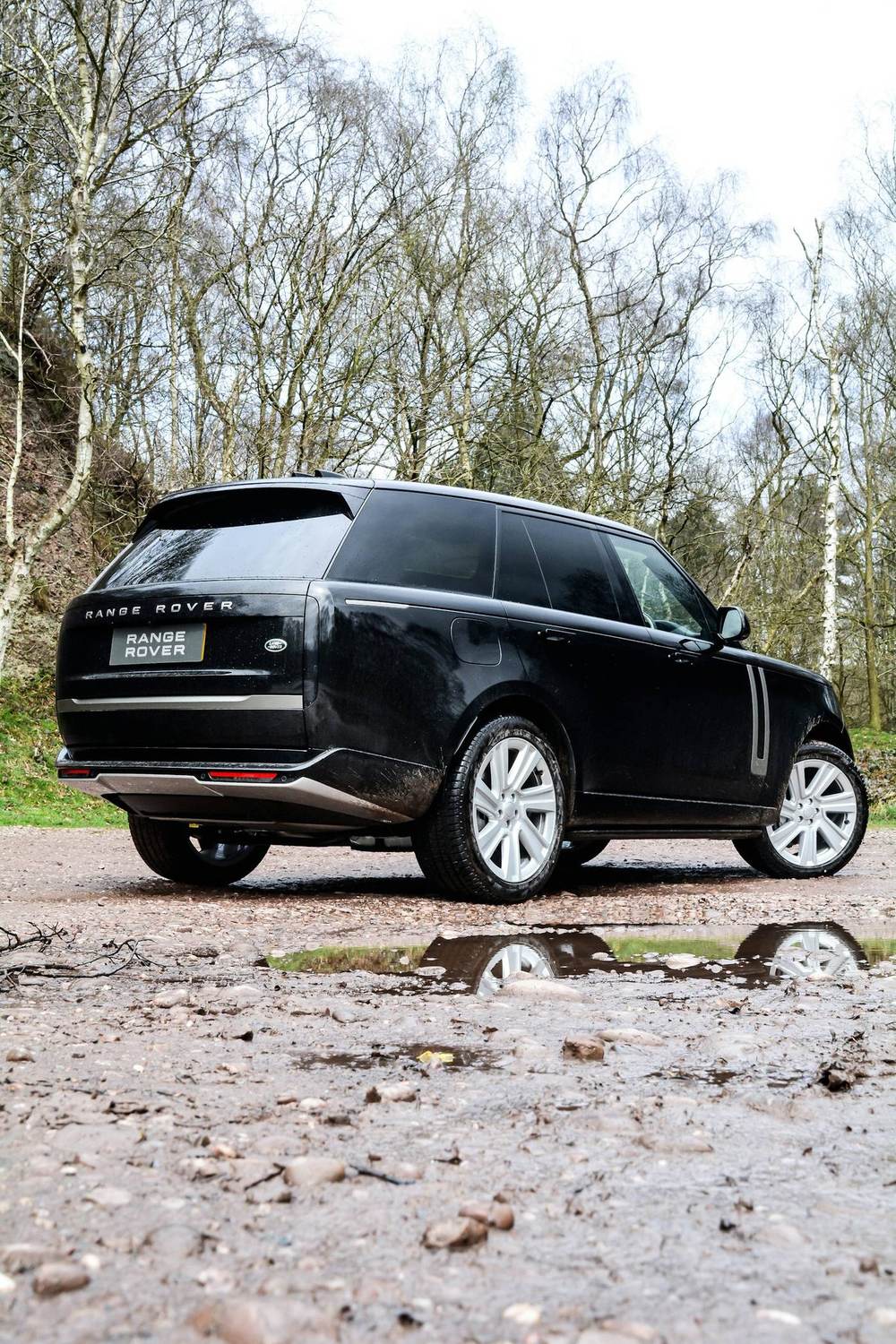 A dark estate vehicle parked on a gravel drive among trees